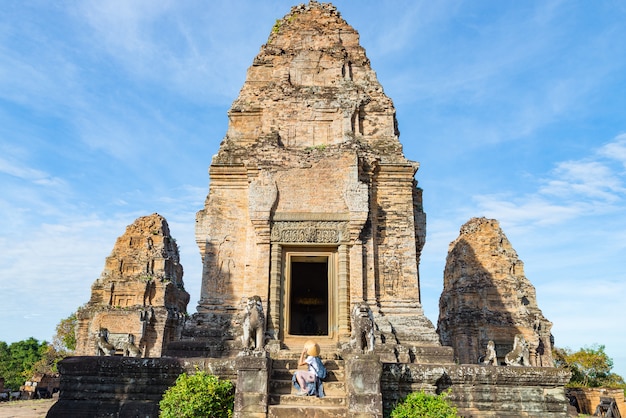Один турист, посещающий руины Ангкора среди джунглей, храмовый комплекс Ангкор-Ват, туристическое направление Камбоджа. Женщина в традиционной шляпе, вид сзади.