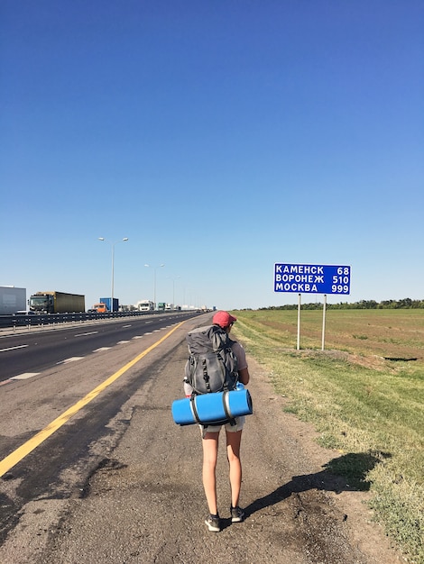 Una ragazza del viaggiatore con uno zaino cammina lungo la strada in una giornata di sole estivo.