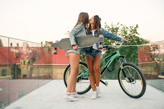 One trendy 30s girl with bike waiting for her hot female friend in tempting shorts on the specially equipped observation deck