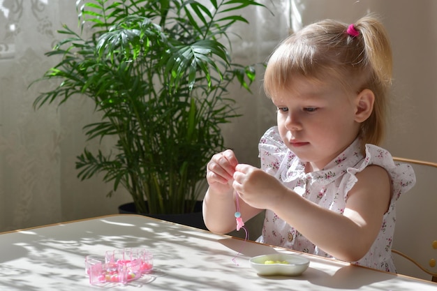 One twoyearold girl is sitting at a table and stringing beads on a string