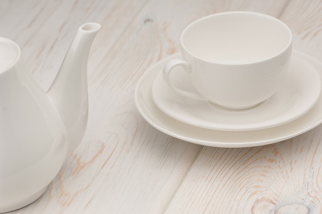 One white cup and saucer and a kettle on an old wooden board