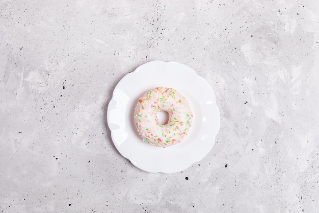 Foto una ciambella bianca vetrata giace su un piatto bianco al centro di uno sfondo di cemento grigio