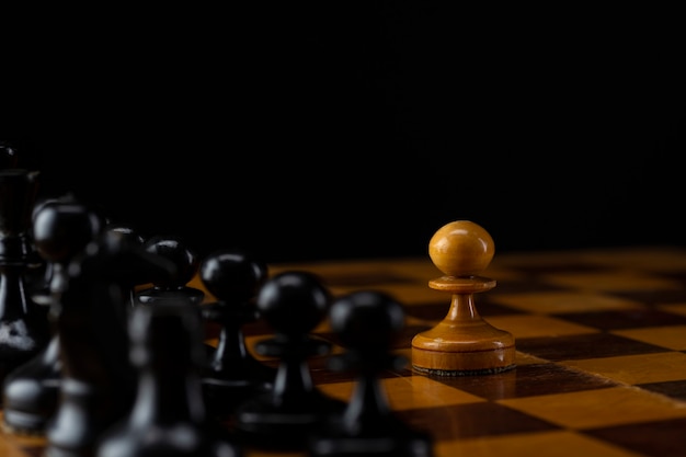 One white pawn against an army of black pieces on a chessboard.