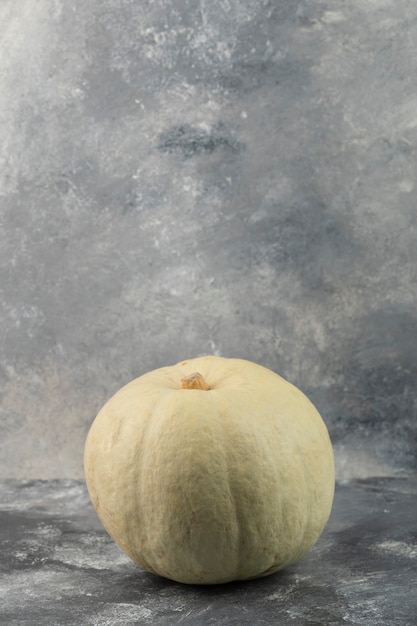 One whole fresh grey pumpkin placed on a marble table . 