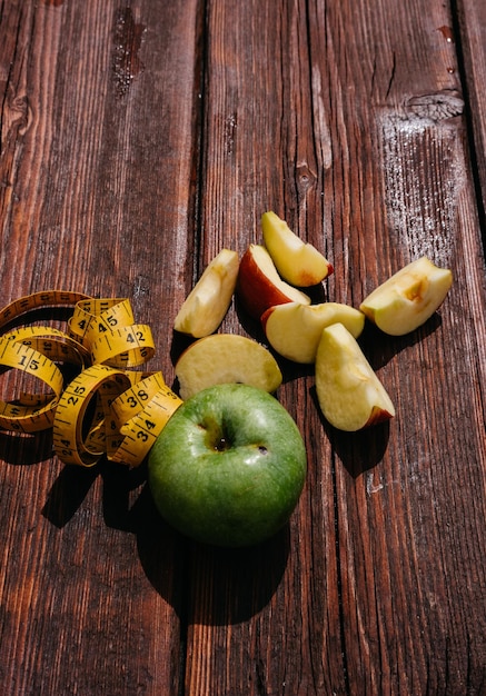 One whole green Apple and a red Apple cut into pieces lie on the wooden kitchen table