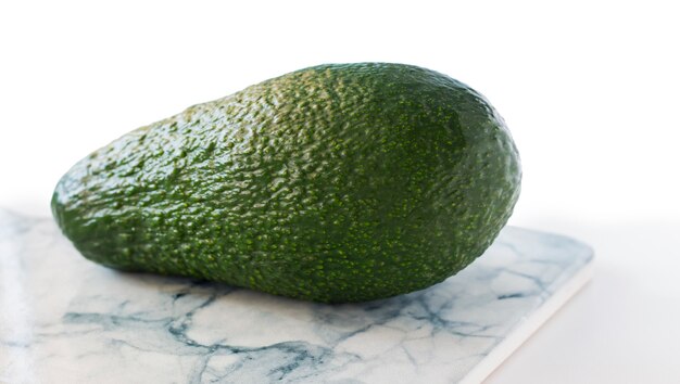 One whole green avocado close up on marble board