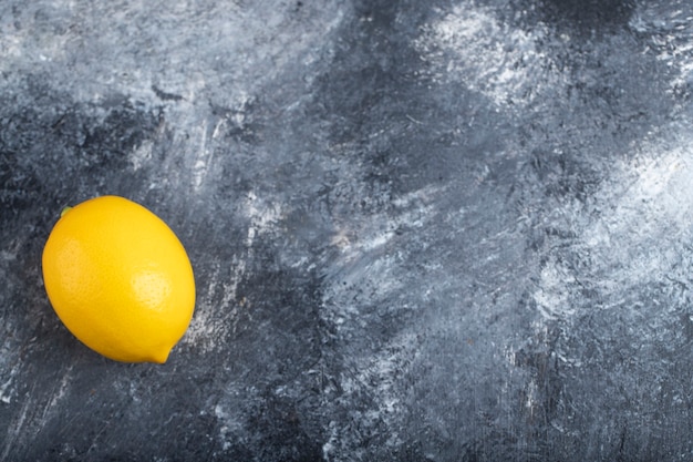 One whole lemon placed on a stone surface 