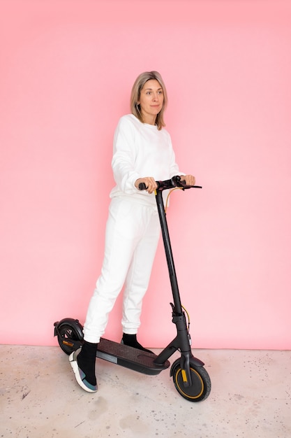 ピンクの背景、スタジオショット、全身写真の電気プッシュスクーターの一人の女性