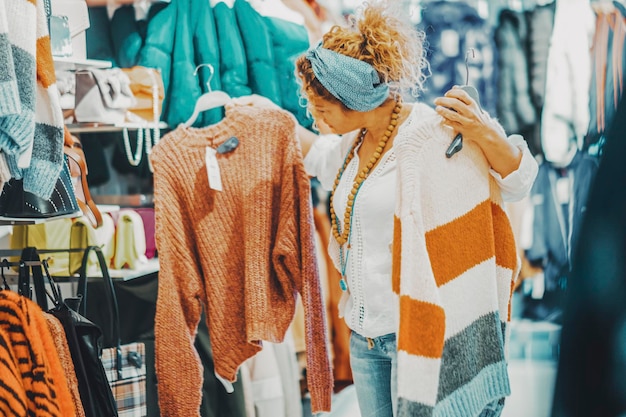 Foto una donna in cerca di abbigliamento in un negozio persone di sesso femminile e lavoro di moda o attività di shopping signora alla moda che cerca un maglione all'interno di un negozio durante le festività natalizie scontate