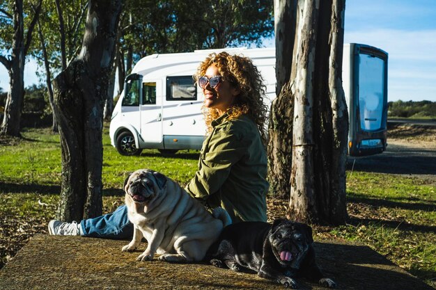 One woman sitting on the ground with her two best friends dogs pug in travel stop with alternative house vanlife motorhome camper in background People and animals owner love concept Outdoor leisure