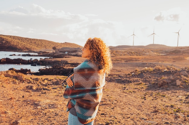 一人の女性が立って抱きしめ、背景と海の海岸にタービン風車のある美しい風景を楽しんでいます.人々のコンセプトは、旅行と冒険のライフスタイルだけが大好きです.