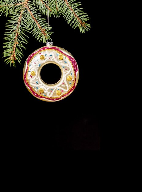 One Xmas decoration colorful glass donut hanging on green fir branches on black vertical backdrop.