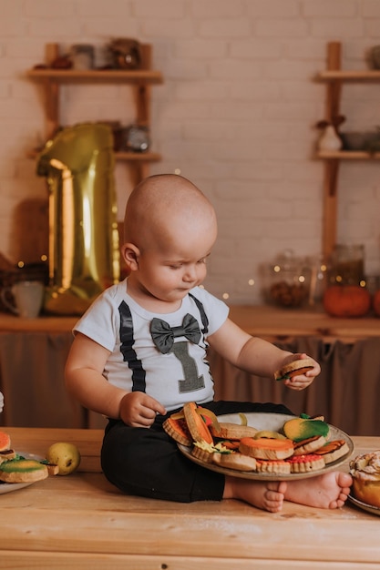 1歳の赤ちゃんが自家製の塗装ジンジャーブレッドを食べます。お祝いの雰囲気の中で最初の誕生日。子供のための健康的なスナック。小さな男の子が台所のテーブルに座っています。高品質の写真