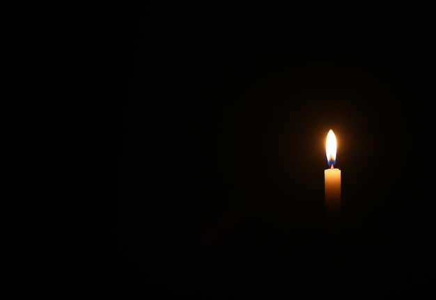 One yellow candle burns in black wall