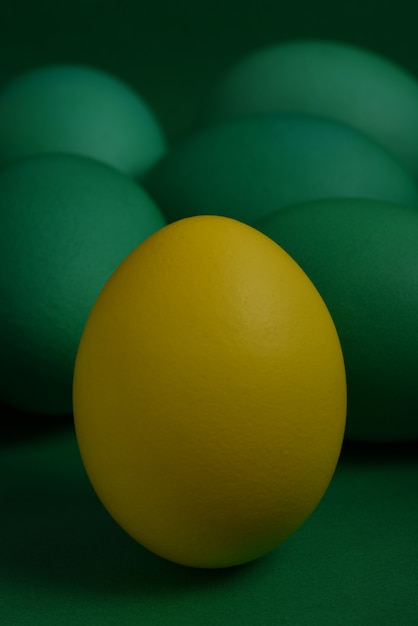 Photo one yellow painted easter egg stands in front of green eggs on a green background