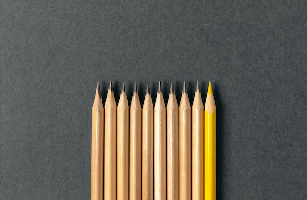 One yellow pencil standing out from the series of gray pencils
