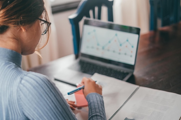 Una giovane bella donna che studia e analizza la grafica sul computer a casa adolescente femminile che fa i compiti sul tavolo con il computer portatile utilizzando internet