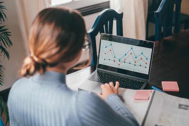 Foto una giovane bella donna che studia e analizza la grafica sul computer a casa adolescente femminile che fa i compiti sul tavolo con il computer portatile utilizzando internet