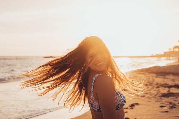 한 젊은 백인 여성이 카메라를 보고 웃고 해변에서 즐거운 시간을 보내고 있습니다. 야외에서 일몰을 즐기는 여성 10대 xA