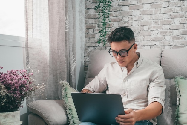 One young happy man surfing the net using his laptop at home sitting on the sofa enjoying free time and relaxing alone Entrepreneur boy working and building his futurexA