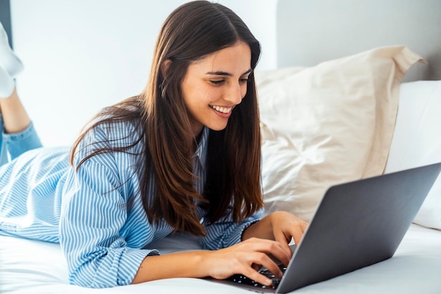 1人の若い女性が自宅で一人でインターネットをサーフィンし寝室でベッドに横たわっている旅行者ビジネスホテルの部屋で働く現代的なオンライン人1人の女性がラップトップコンピュータをリラックスで使用している