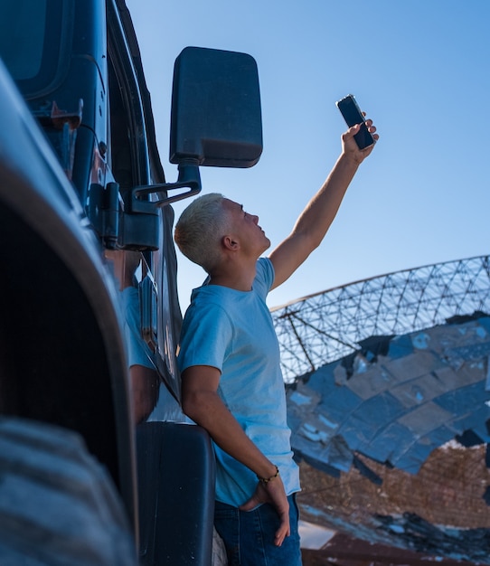 One young man or teenager looking for signal with his phone and car - millennial addicted at phone in the nowhere looking for connection - blonde hair adult