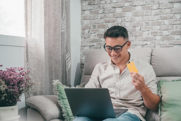 Un giovane uomo che utilizza il laptop e acquista sul negozio online ragazzo felice che utilizza la carta di credito per effettuare acquisti da internet