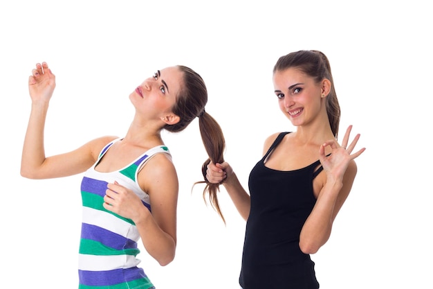 One young positive woman in black shirt holding another womans hair and showing OKAY in studio