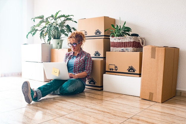 One young woman and happy people after buy a new house or apartment together to live together - person on the ground using laptop with boxes ad packs on their back