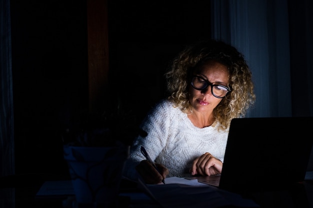 One young woman using laptop and working on a computer at night at home. Businesswoman at job in his office