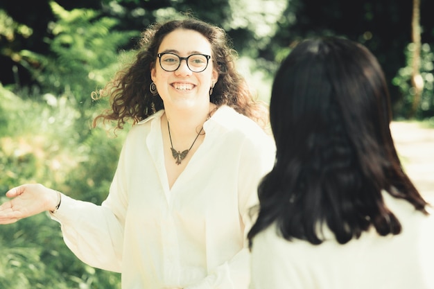 One young woman with glasses smiling and explaining something to a friend during a sunny day