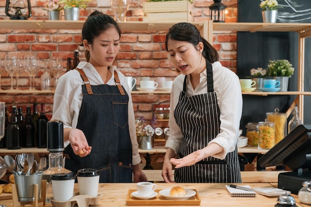 Onervaren meisjesbarista. boze eigenaar van restaurant berispt nieuwe werknemer achter toog. manager ontevreden over het werk van de serveerster om koffie te zetten en croissants te bakken in een moderne caféwinkel.