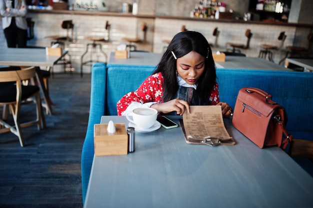 Сonfident young african american woman in smart casual wear at cafe read menu