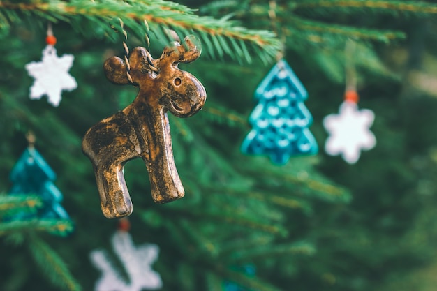 Ongebruikelijk keramiek speelgoed in de vorm van een eland, een kerstboom en sneeuwvlokken hangen aan een sparren tak. Decoraties voor het nieuwe jaar, feestelijke stemming