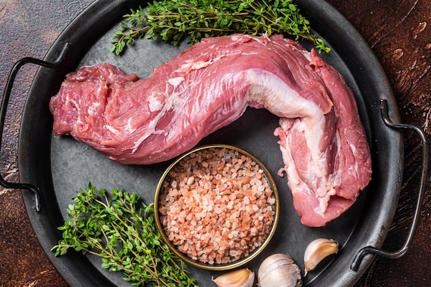 Ongekookt Rauw varkenshaasfiletvlees op een keukenblad met tijm, knoflook en zeezout Donkere achtergrond Bovenaanzicht