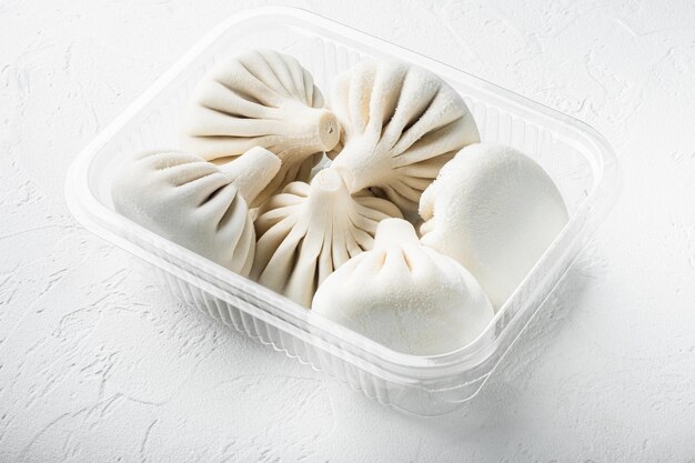 Ongekookte Baozi chinese knoedels Aziatische knoedels in plastic bakje op witte stenen ondergrond