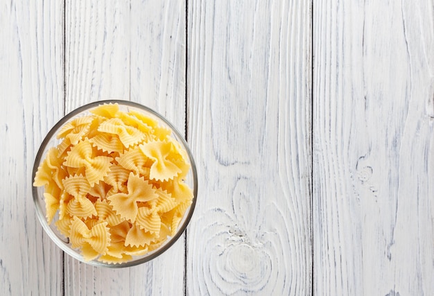 Ongekookte farfalle pasta in glazen kom op witte houten tafel met uitknippad