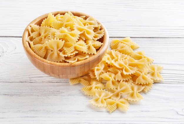 Foto ongekookte farfalle rigate pasta in houten kom op witte houten achtergrond