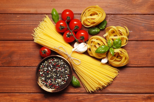 Ongekookte fettuccine bal, verschillende pasta, ingrediënten voor saus. kerstomaatjes, kruiden, olie, basilicum op een houten ondergrond. bovenaanzicht. Plaats voor tekst.
