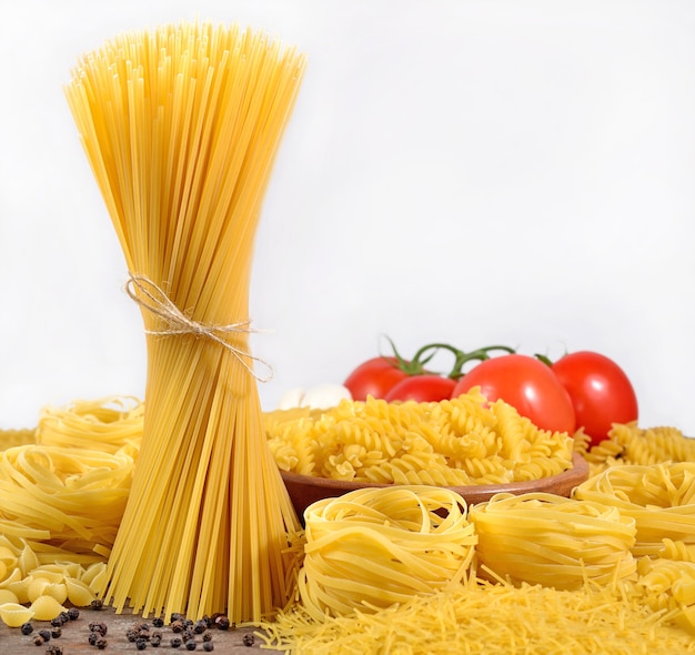 Ongekookte Italiaanse deegwaren, rijpe tomatentak en zwarte peper op een witte achtergrond