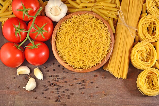 Ongekookte Italiaanse pasta, rijpe tomatentak, knoflook en zwarte peper op een houten ondergrond