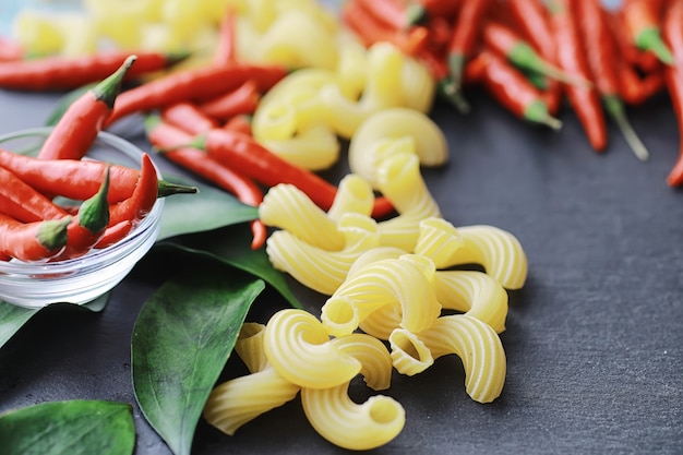 Ongekookte pasta op een stenen achtergrond. Met kruiden en specerijen, pittige chilipepers en specerijen.