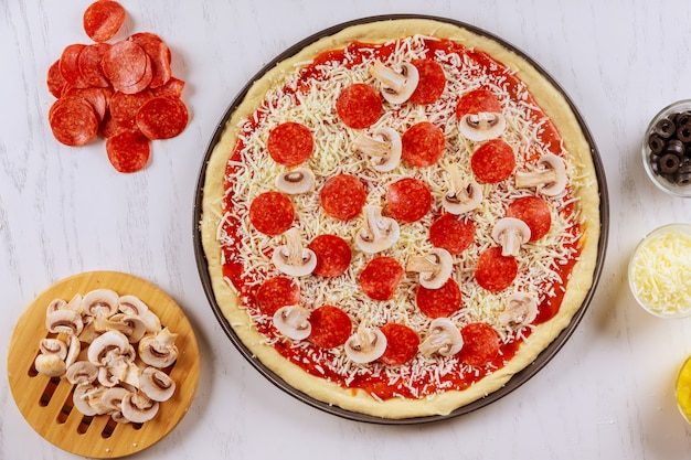 Ongekookte pizza met pepperoni en champignons.