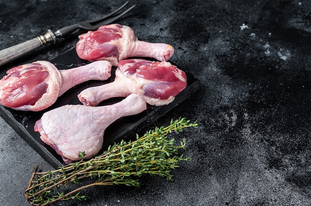 Ongekookte Rauwe Eendenpoten drumsticks op marmeren bord. Zwarte achtergrond. Bovenaanzicht. Ruimte kopiëren.