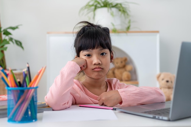 Ongelukkig klein blank meisje dat thuis aan tafel zit, voelt zich lui, ongemotiveerd en doet huiswerk. Verstoord, verontrust klein 7-jarig kind bereidt schooltaak voor, leert studeren met boeken. Onderwijsconcept.