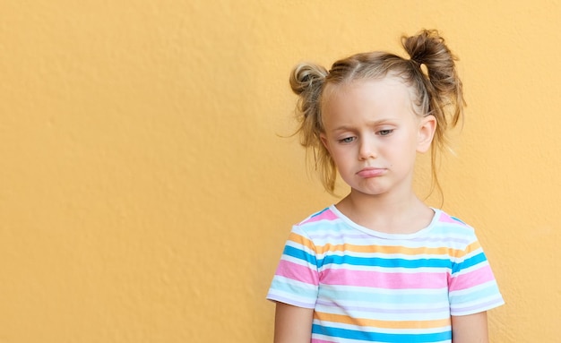 Ongelukkig klein meisje geïsoleerd over gele studio achtergrond negatieve emoties en gevoelens