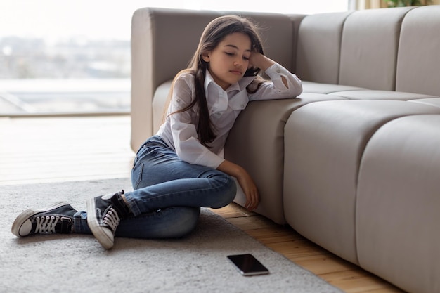 Ongelukkig meisje zit in de buurt van smartphone die lijdt aan digitale depressie binnenshuis