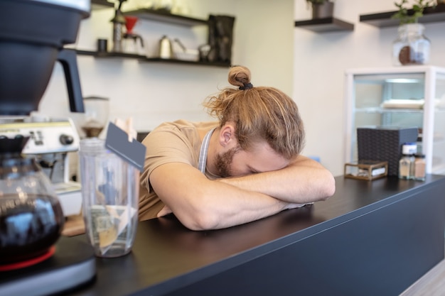 Ongelukkig moment. Langharige man met zijn hoofd op handen die zijn gezicht achter toog in café verbergt