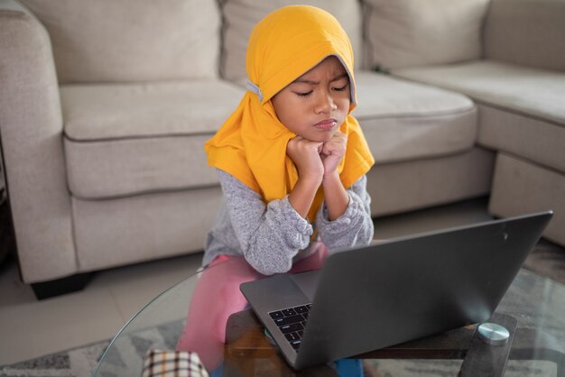 Ongelukkig moslim jong kind tijdens het studeren vanuit huis met behulp van laptop