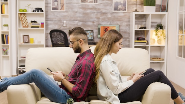 Ongelukkig paar rug aan rug op de bank zitten. Paar ingoring elkaar met behulp van telefoons.